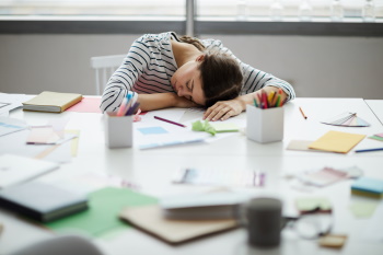 Portrait of young woman napping on table at work. 
